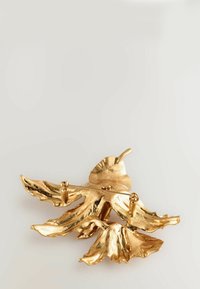 Goldfarbener Brosche in Blattform, mit strukturierten Details und zwei Stecknadeln zur Befestigung, die eine natürliche Designästhetik widerspiegelt.