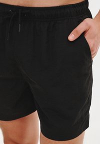 Czarne szorty wykonane z lekkiego materiału, z elastycznym pasem ze sznurkiem i bocznymi kieszeniami. Gładka faktura i casualowy design.