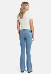 Jeans svasati azzurri chiari con vita media e due tasche posteriori. Abbinati a una T-shirt aderente a maniche corte color crema.