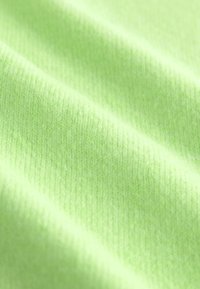 Tissu tricoté doux vert clair avec une texture de tissage fin visible et des plis doux créant des ombres diagonales.
