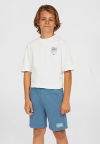 T-shirt blanc à manches courtes avec un graphique bleu sur la poitrine, associé à un short bleu avec un logo. Les deux sont fabriqués en tissu doux.