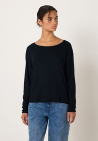 Svart långärmad topp med bred, rund halsringning, gjord av en slät tyg. Kombinerad med ljusblå högmidjade jeans.