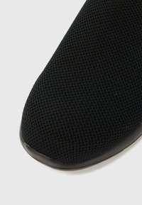 Czarna dzianinowa cholewka buta z elastyczną, fakturowaną powierzchnią; zaokrąglony czubek i kontrastowa czarna podeszwa. Monochromatyczny design z minimalnymi detalami.