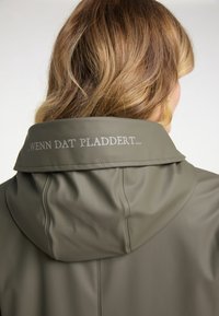 Olivově zelená voděodolná bunda s kapucí, na límci s stříbřitým potiskem a hladkou, lesklou strukturou.