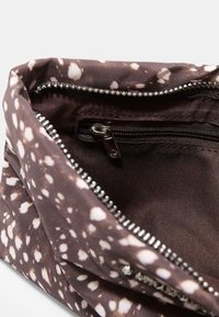 Pochette en tissu marron avec un motif à pois blancs, zip argenté ouvert et poche intérieure zippée visible.