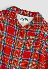 Røde flannel pyjamas med blå, grønne og gule tern. Har en rund krave, brystlomme og orange knapper. Mærkeetiket synlig.