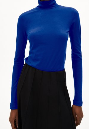 Top azul de manga larga y cuello alto, confeccionado con una tela suave y lisa, combinado con una falda negra plisada. El diseño presenta una silueta ajustada.