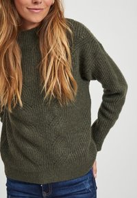 Pull en maille de couleur vert olive foncé avec une texture côtelée et un motif en tricot torsadé à l'avant. Dispose d'un col rond et de manches longues.