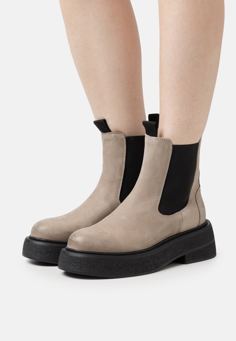 Bottes de cheville en daim marron avec des panneaux latéraux en élasthanne noir et une épaisse semelle en caoutchouc noir. Bout rond et détails de couture minimaux.