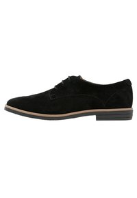 Scarpe lace-up in suede nero con tacco basso a blocco, punta tonda e suola beige a contrasto. Texture liscia con dettagli minimi.