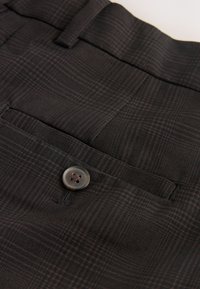 Primo piano di pantaloni scuri a quadri che mostrano la cintura, la passanti della cintura, la tasca posteriore con bottone e la fine texture del tessuto.