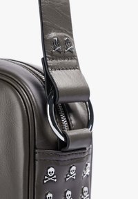 Bolso de cuero sintético gris con acentos de calavera y huesos cruzados en plata, cierre de cremallera y una correa resistente con un detalle de anillo metálico.