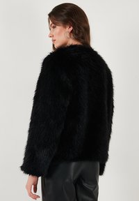 Black faux fur jacket with a soft, textured finish, featuring long sleeves and a rounded hem. Worn over black leather pants.