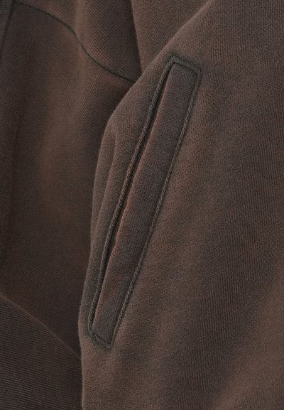 Sweat-shirt marron avec un tissu texturé, une poche sur la couture latérale, des bords cousus et une apparence douce et confortable.