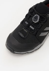 Black athletic shoe featuring a textured upper, bungee lacing system, Gore-Tex branding, and reflective grey accents on the side.