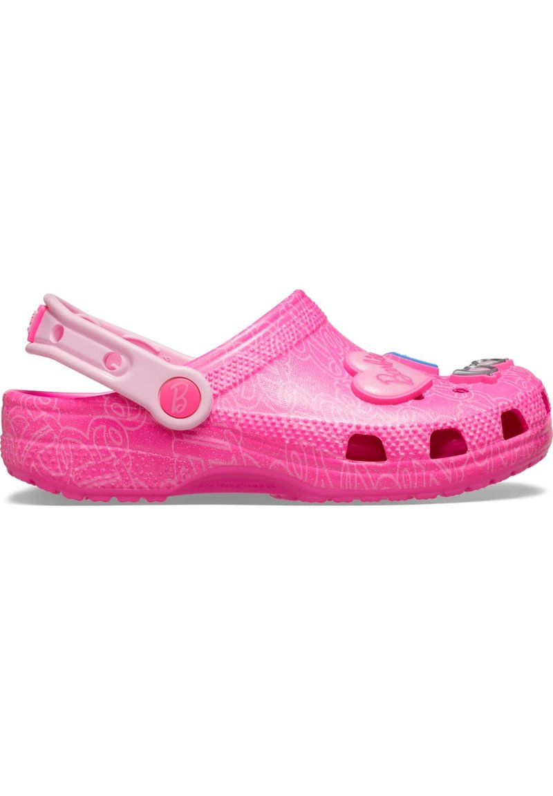 Ρυθμιζόμενες ροζ πλαστικές παντόφλες με κομμένες τρύπες, υφή στην επιφάνεια και ρυθμιζόμενο λουράκι στη φτέρνα. Διαθέτουν διακοσμητικά στοιχεία σ την μπροστινή πλευρά.