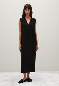 Schwarzes ärmelloses Kleid mit tiefem V-Ausschnitt und gerader Silhouette, aus weichem Stoff gefertigt. Verfügt über seitliche Schlitze für Bewegungsfreiheit.