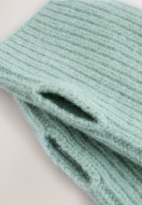 Accessoire en laine douce tricotée couleur menthe, présentant une texture côtelée et deux ouvertures. Finement confectionné avec un aspect chaleureux.