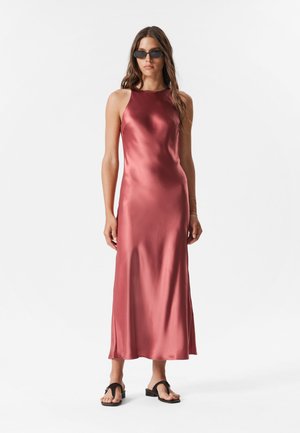 Satin-Midi-Kleid in tiefem Rosenrot, mit taillierter Oberseite, ohne Ärmel und fließendem Rock; kombiniert mit schwarzen Flip-Flops.