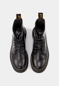 Bottes en cuir noir avec bout rond, coutures jaunes, lacets à l'avant et col rembourré. Présente une boucle de marque au talon.