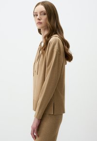 Beige hoodie van zachte stof, met een relaxed fit, ribgebreide onderrand, koord en zijsplitten voor comfort en stijl.