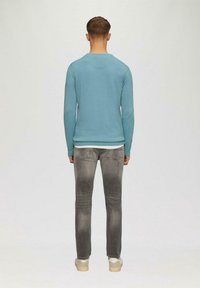 Hellblaues langärmeliges Sweatshirt, graue Jeans und beige Schuhe von hinten betrachtet. Das Sweatshirt hat einen runden Halsausschnitt und enganliegende Bündchen.