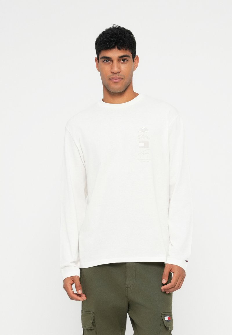 Λευκό πουκάμισο μακρυμάνικο με στρογγυλή λαιμόκοψη, με εκτύπωση γραφικών μπροστά. Συνδυάζεται με ελαιοπράσινα cargo παντελόνια. Υλικό από βαμβάκι.