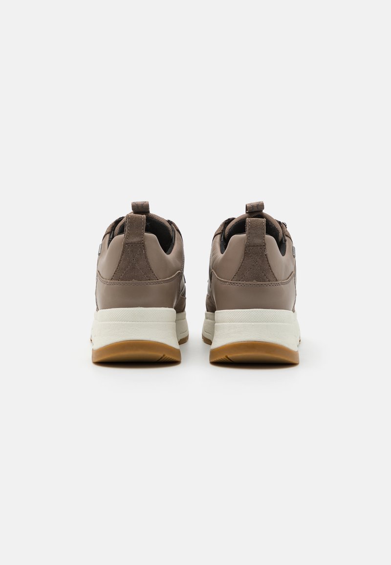 Scarpe da ginnastica marroni con una tomaia in pelle liscia e dettagli in camoscio. Presentano una soletta bianca e una suola in gomma color caramello. Anello di trazione sul tallone.