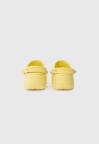 Yellow clogs with a smooth, matte finish. Features adjustable back strap and drainage holes. Textured sole for grip. Branding visible on strap.