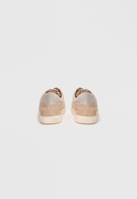 Low-top sneakers featuring a beige suede material with textured silver accents on the upper, rounded shape, and a light-colored rubber sole.