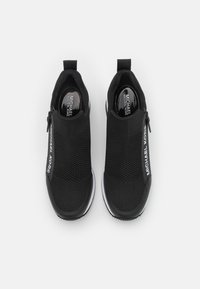Sorte treningssko med overdel i strikket mesh, slip-on design og glidelåslukking. Har hvit merking på siden og gummisåle med godt grep.