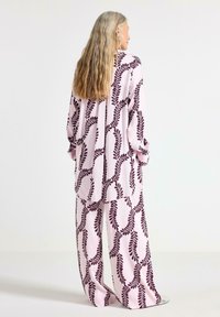 Completo pigiama rosa chiaro composto da una maglietta a maniche lunghe e pantaloni a gamba larga, decorato con un motivo a foglia bordeaux scuro e una texture liscia.
