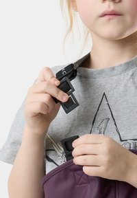 Purple bag with a textured finish, featuring black adjustable straps and plastic buckles, held by a child in a gray shirt with a design.