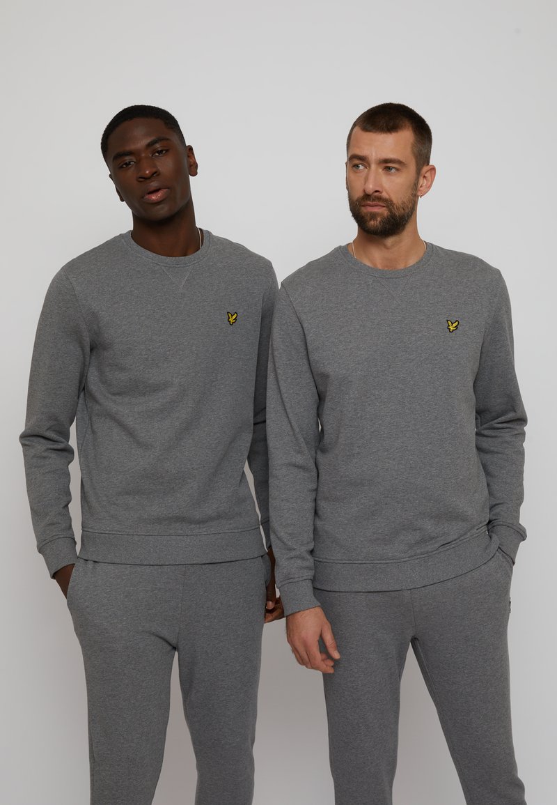 Des sweatshirts gris et des pantalons assortis en tissu doux, arborant un petit logo jaune sur la poitrine. Look décontracté et coupe relax avec des poignets côtelés.