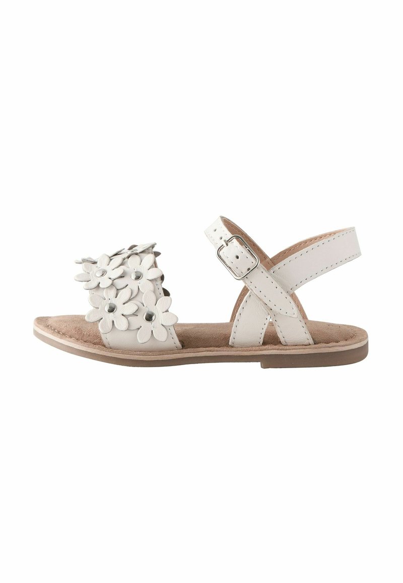 Sandal bianco con decorazioni floreali sulla parte anteriore, cinturino alla caviglia regolabile e suola piatta. Texture morbida e design minimalista.