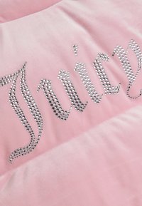 Roza velur tkanina s velikim kristalnim natpisom "Juicy." Glatka tekstura s sjajnim dekorativnim elementom. Suptilno vidljivo šivanje.
