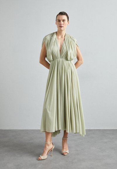 Rochie verde deschis cu decolteu adânc în V, mâneci scurte și un design plisat. Asortată cu sandale cu toc nude. Țesătură netedă și fluidă.