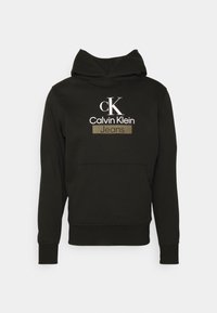 Svart Calvin Klein-hoodie med framficka och logotexten "cK Calvin Klein Jeans" i vitt och beige på bröstet.