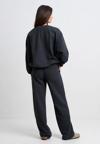 Bluza na suwak w ciemnoszarym kolorze oraz dopasowane spodnie z miękkiego materiału. Strój ma luźny krój i ściągacze na rękawach i nogawkach. Charakterystyczny ze względu na prostotę i wygodę.