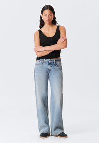 Ljust blå denim flare-jeans med hög midja, med en blekt finish och fem fickor. Matchas med en svart linne.