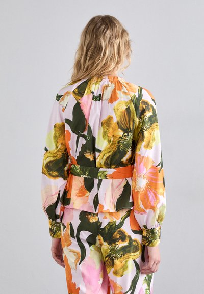 Blusa floreale colorata con maniche lunghe, scollatura arricciata e vita peplum. Presenta motivi vivaci nei colori rosa, arancione e verde.