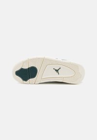 Valge alusega sneakerite tald, mis on varustatud tekstuuriga rohelise kummist aktsendiga ja logoga. Siin on diagonaalsed sooned ja ringikujulised mustrid.