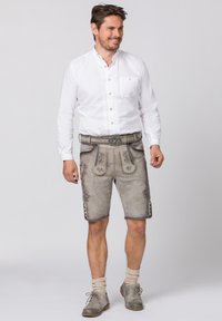 Grijze leren lederhosen met bloemenborduursel, gedragen met een witte overhem genoemd shirt. Voorzien van een riem met een decoratieve gesp en een knielange snit.