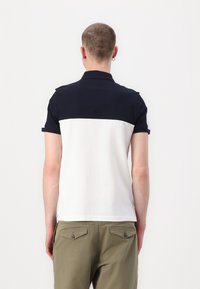 Marineblå og hvit polo skjorte med korte ermer og krage. Har et to-farget design med strukturert stoff og strømlinjeformet fasong.