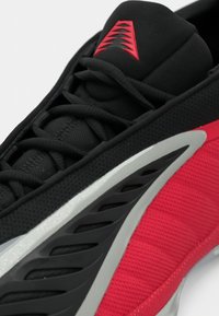 Αθλητικό παπούτσι με μαύρο άνω μέρος από δίχτυ, κόκκινα υφασμάτινα στοιχεία και λείο γκρι ενδιάμεσο πέλμα. Διαθέτει περίτεχνο κορδόνι και τολμηρές γραμμές σχεδίασης.