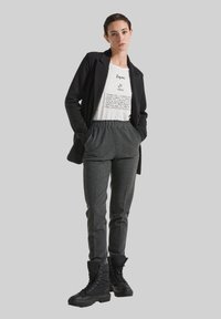 Schwarze Blazer über einem weißen Graphic-T-Shirt, kombiniert mit grauen karierten Hosen und schwarzen Combat-Boots. Das Outfit zeichnet sich durch eine lockere Passform und einen lässigen Stil aus.