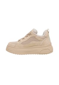 Chaussure de sport beige avec tige en mesh et daim, doublure moelleuse, semelle en caoutchouc épaisse et accents texturés contrastés. Détail du logo visible sur le côté.