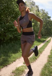 Graues Sporttop mit schwarzen Akzenten, passende graue Shorts, schwarze Turnschuhe und dunkle knielange Socken, getragen von einer Person, die auf einem Weg läuft.