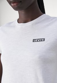 Bílý bavlněný tričko s kulatým výstřihem a malým černým logem Levi's na levé části hrudníku. Hladký materiál, standardní střih.