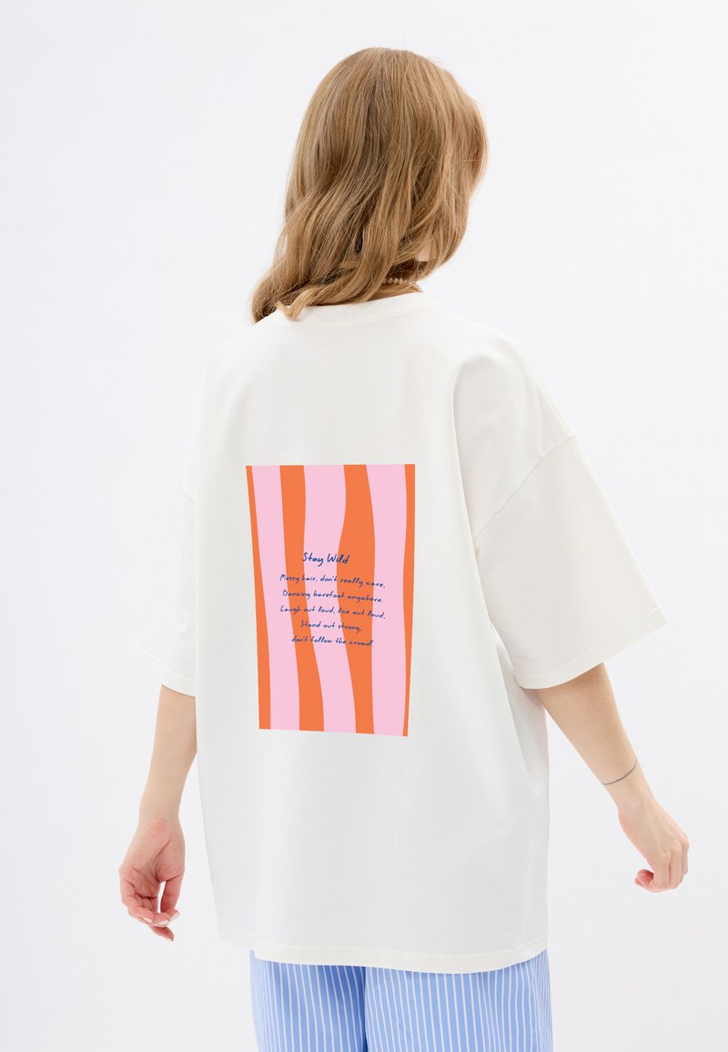 Witte oversized t-shirt met een rechthoekige grafiek in roze en oranje strepen en blauwe tekst op de achterkant. Korte mouwen en een relaxte pasvorm.